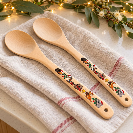 Two Australian Christmas wooden spoons on a tea towel beside eucalyptus and festive lights.