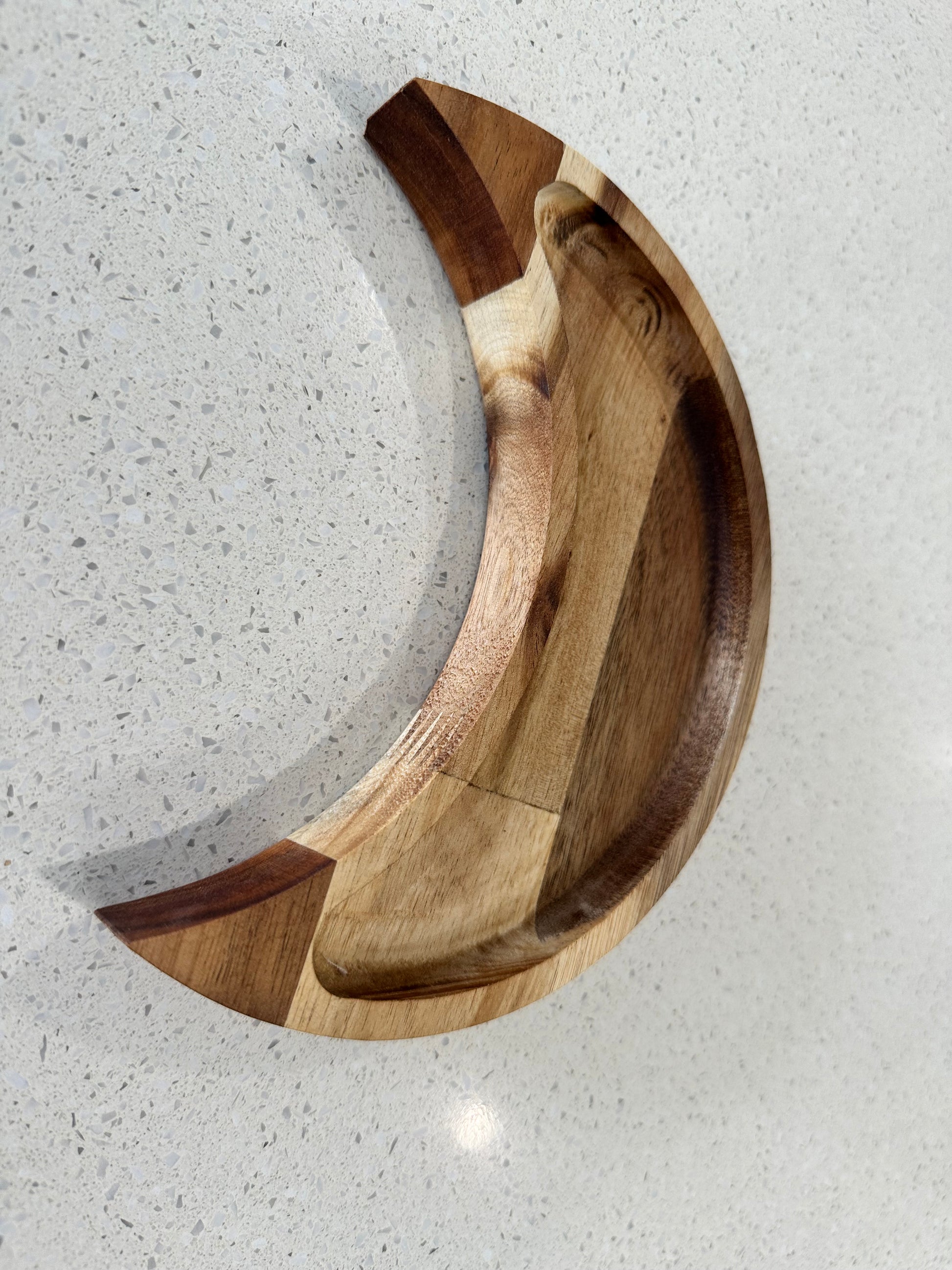 A crescent-shaped acacia wood jewelry tray with a natural finish, placed on a white surface.