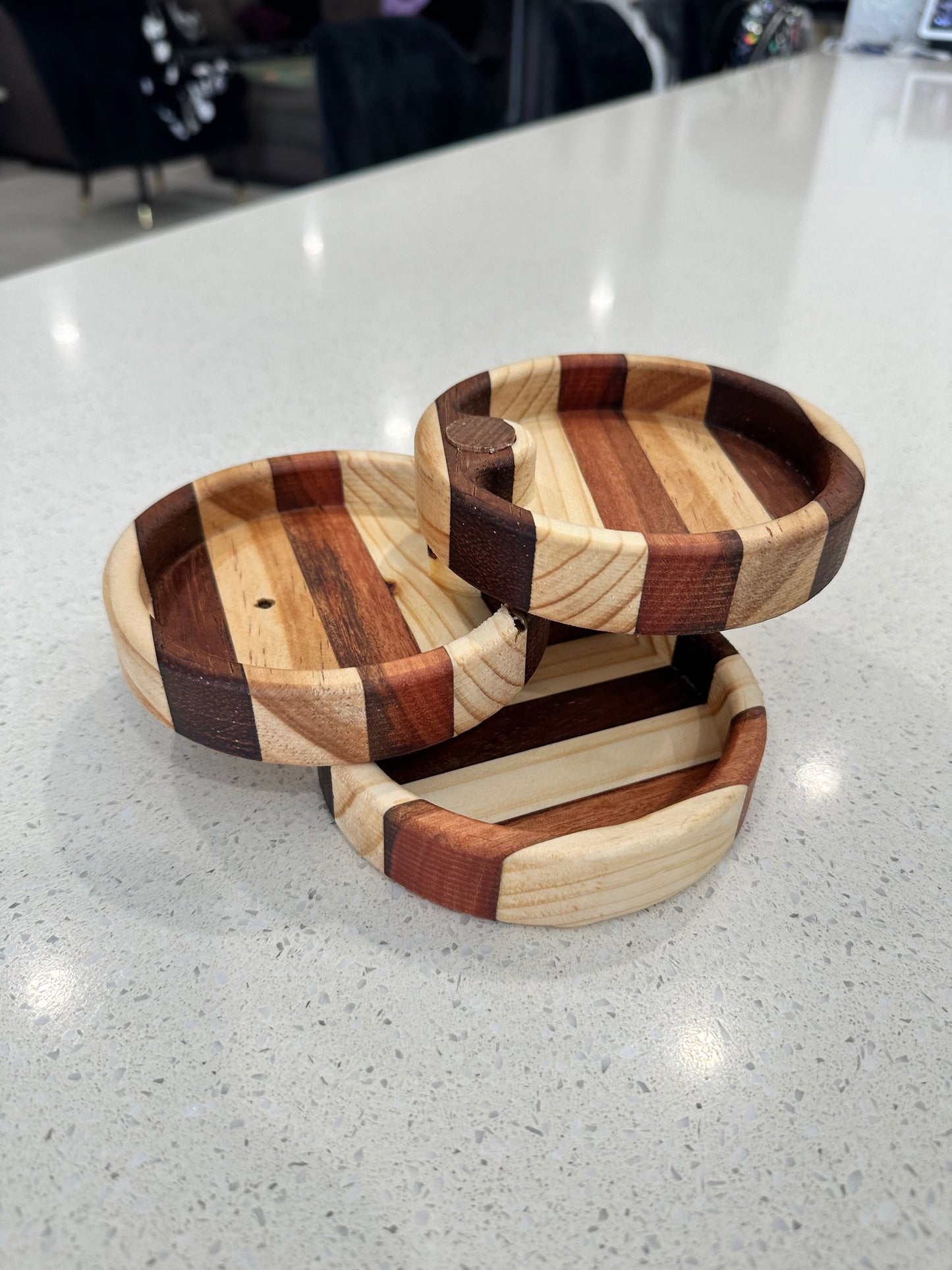 A three-tiered, circular fold-out jewelry holder made of wood, placed on a countertop.