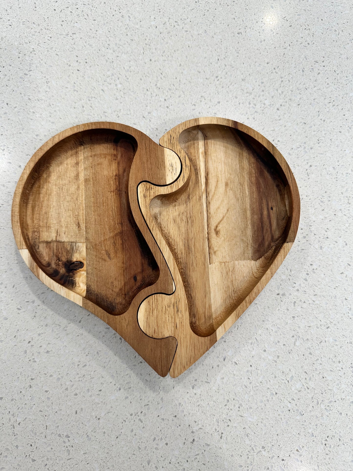 A heart-shaped acacia wood jewelry tray, with a puzzle-like interlocking design, displayed on a white surface.