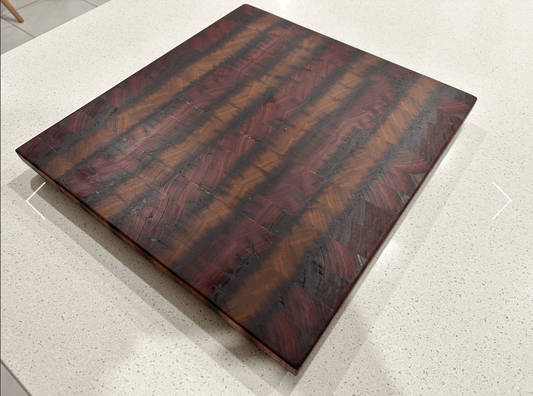 A rectangular Spotted Gum wood cutting board with a striped grain pattern, placed on a light surface.